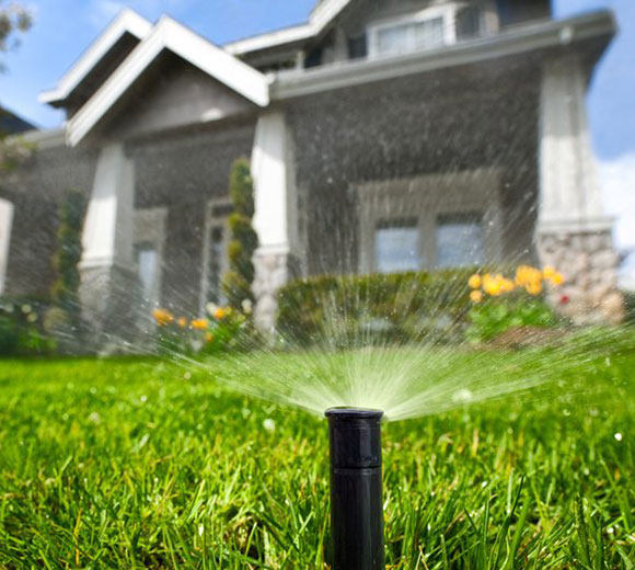 Popup lawn sprinkler head in the foreground and out of focus home in the background.